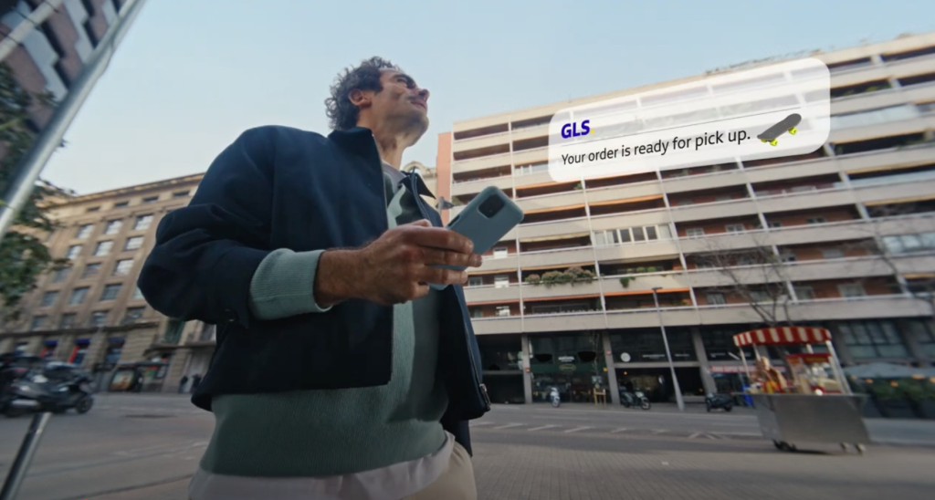 Un uomo in città guarda lo smartphone e riceve una notifica GLS con la scritta “Your order is ready for pick up”. Frame tratto dallo spot della campagna Out of Home GLS, che racconta con tono diretto e moderno l’efficienza e la semplicità del servizio di consegna.
