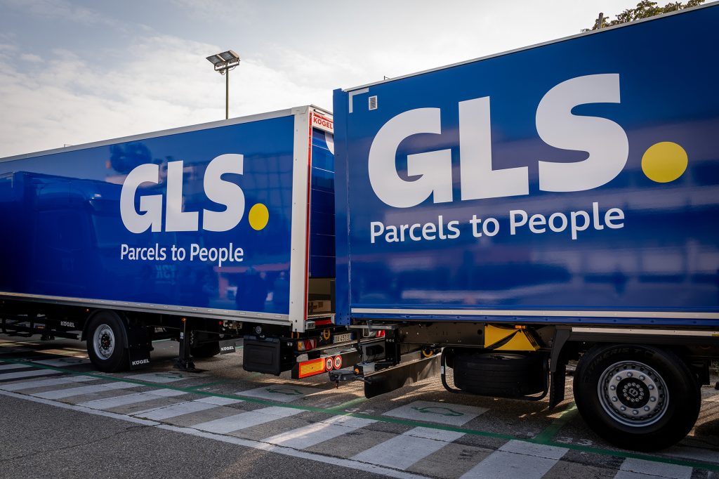 Due furgoni blu con la scritta “GLS” e “Parcels to People” in bianco e giallo, parcheggiati uno accanto all'altro